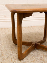 Load image into Gallery viewer, A close-up of a mid-century modern wooden side table with a warm medium-brown finish, featuring a star-shaped base and a light-colored woven rug underneath.