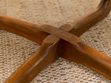 Load image into Gallery viewer, Close-up of a four-armed wooden table base with a polished warm brown finish, resting on a woven beige rug.
