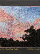 Load image into Gallery viewer, A square textile artwork or tapestry depicting a colorful sky with pink, peach, blue, and lavender tones above dark tree silhouettes. The piece has a dark charcoal border with embroidered text reading 'Sky Conditions, Cuba' and 'Marlyn Isbell' at the bottom.