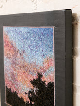 Load image into Gallery viewer, A square canvas wall art print with a dark charcoal gray border, featuring a textured, painterly sky in shades of blue, pink, and purple above black tree silhouettes, shown leaning against a white brick wall.