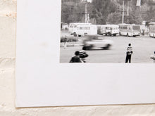 Load image into Gallery viewer, A black and white photographic art print mounted on a textured white brick wall. The print features a vintage scene with buses, a car, and people, styled with a wide white border.