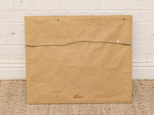 Load image into Gallery viewer, A square tan paper or fabric panel with a single black cord stretched horizontally across the center, photographed against a white painted brick wall and woven floor mat.