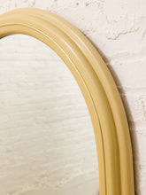 Load image into Gallery viewer, A close-up of a curved, ribbed mirror frame in a warm mustard yellow or pale gold finish, leaning against a textured off-white brick wall.