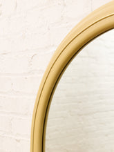 Load image into Gallery viewer, Close-up of a round wall mirror with a curved, double-trimmed frame in a warm mustard yellow or ochre color, set against a white painted brick wall.