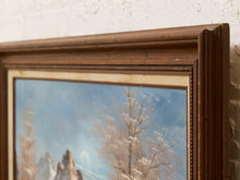 Load image into Gallery viewer, A close-up of a framed landscape painting showing snow-covered trees and mountains under a blue sky, with a dark brown wooden frame and a cream mat against a textured off-white wall.