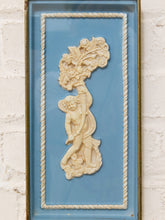 Load image into Gallery viewer, A framed decorative wall piece featuring a cream-colored relief sculpture of a cherub holding a floral branch, set against a light blue background with a rope-style border and gold-toned frame, mounted on a white brick wall.