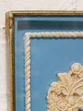 Load image into Gallery viewer, Close-up of a framed decorative wall piece with a blue background, cream rope border, and carved floral ornament, shown against a white textured wall.