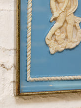 Load image into Gallery viewer, Close-up of a framed decorative wall art piece with a light blue background, cream sculpted figure detail, rope-style border, and a distressed metallic frame against a white textured wall.