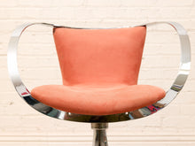 Load image into Gallery viewer, A modern barstool with a curved chrome tubular steel frame and a peach-colored suede seat and backrest, set against a white brick wall background.