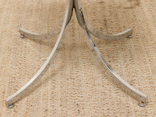 Load image into Gallery viewer, Close-up of a polished silver metal table base with three curved legs, resting on a textured beige woven rug.