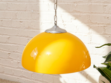 Load image into Gallery viewer, A glossy yellow dome pendant light hanging from a silver chain against a white brick wall with sunlight and leaf shadows.