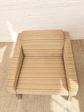 Load image into Gallery viewer, A modern armchair with beige and brown striped upholstery, positioned on a textured rug against a white brick wall.