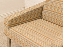 Load image into Gallery viewer, Close-up of a striped upholstered armchair in beige, tan, brown, and muted blue tones, with a light cream wall and textured rug visible.