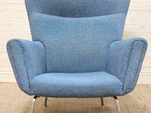 Load image into Gallery viewer, A mid-century modern high-back lounge chair upholstered in textured blue fabric, featuring curved armrests and slim chrome legs, set against a white brick wall and beige jute rug.