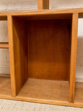 Load image into Gallery viewer, Close-up of the interior of a wooden shelf or cabinet with warm medium-brown wood grain, set against a white brick wall and light woven rug.
