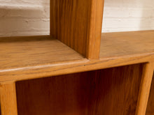 Load image into Gallery viewer, Close-up of a warm medium-brown wooden shelf or cabinet corner with a white painted brick wall background.