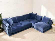 Load image into Gallery viewer, A modern L-shaped sectional sofa upholstered in deep blue velvet fabric, styled in a minimalist room with a white brick wall and light beige carpet.