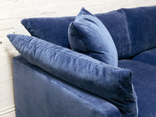 Load image into Gallery viewer, A close-up of a blue velvet sofa with matching throw pillows, set against a white painted brick wall.