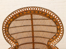 Load image into Gallery viewer, Close-up of a woven rattan chair back with a scalloped, openwork border and a central vertical support, set against a white painted brick wall.
