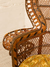 Load image into Gallery viewer, Close-up of a woven rattan chair with a curved armrest, featuring a natural brown and black patterned weave, set against a light beige wall and carpet.