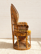 Load image into Gallery viewer, A tall, sculptural rattan chair with a high back, woven basketweave details, and a small yellow cushion on the seat, photographed against a white brick wall.