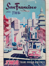 Load image into Gallery viewer, Vintage-style San Francisco travel poster featuring a pink cable car on a city street, with the text 'San Francisco via TWA' and 'TWA Trans World Airlines' at the bottom. The artwork includes buildings, a bridge, and an airplane in the sky, shown against a light brick background.