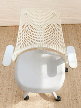 Load image into Gallery viewer, A white mesh office chair viewed from above, positioned on a beige woven rug against a white brick wall.