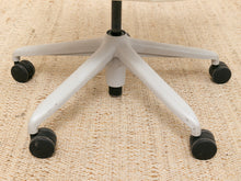 Load image into Gallery viewer, Close-up of a white five-star rolling office chair base with black casters on a woven beige rug.