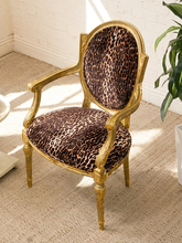 Load image into Gallery viewer, An elegant accent chair with a carved gold frame and leopard-print upholstery, set on a beige carpeted floor in a bright room.