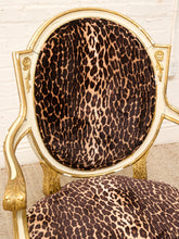 Load image into Gallery viewer, An ornate gold-framed chair with leopard-print fabric upholstery, shown in a close-up view against a white brick wall background.