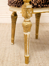 Load image into Gallery viewer, Close-up of an ornate gold-finished chair leg with distressed white paint showing through, next to a leopard-print upholstered seat cushion on a textured beige rug.