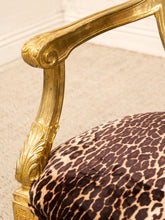 Load image into Gallery viewer, Close-up of an ornate gold armchair with a leopard-print upholstered seat cushion, set against a neutral beige carpeted floor and white wall.
