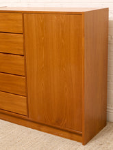 Load image into Gallery viewer, A mid-century modern wooden dresser with a warm honey-brown finish, featuring five drawers on the left and a single cabinet door on the right, set against a white brick wall and beige carpet.