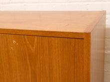 Load image into Gallery viewer, Close-up of a warm medium-brown wooden cabinet corner with visible grain and a few small scuffs, set against a white painted brick wall.