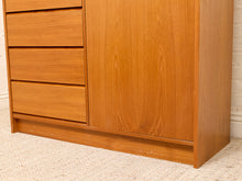 Load image into Gallery viewer, A close-up of a mid-century modern wooden cabinet or dresser with a warm honey-toned finish, featuring three drawers on the left and a single door on the right, set against a white brick wall and light beige carpet.