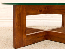 Load image into Gallery viewer, Close-up of a mid-century modern wooden coffee table base with a green glass top, set on a textured beige rug against a white brick wall.