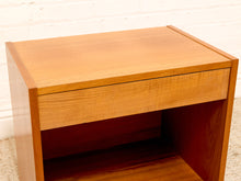 Load image into Gallery viewer, A mid-century modern wooden nightstand with a single drawer and open shelf, made of warm medium-brown wood with a visible grain, set against a white brick wall and light carpet.