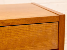 Load image into Gallery viewer, Close-up of a warm medium-brown wooden furniture piece, showing the wood grain on the drawer front and top edge against a light neutral background.