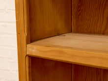 Load image into Gallery viewer, Close-up of a warm honey-toned wooden shelf unit showing the wood grain, corner joint, and shelf edge against a white brick wall background.