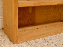 Load image into Gallery viewer, Close-up of a light natural wood shelf or bookcase corner with an open cubby, resting on a woven beige rug against a white wall.