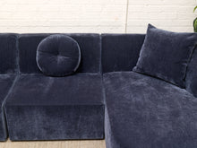 Load image into Gallery viewer, A dark navy blue velvet sectional sofa with matching throw pillows, set against a white brick wall background.