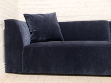 Load image into Gallery viewer, A navy blue velvet loveseat sofa with a matching square throw pillow, set against a white brick wall and light beige carpet.