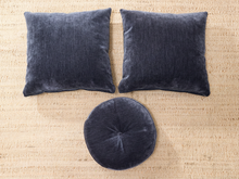 Load image into Gallery viewer, Three dark charcoal gray velvet home decor pieces, including two square throw pillows and one round pouf, arranged on a beige woven jute rug.