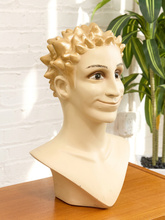 Load image into Gallery viewer, A beige mannequin head and upper torso bust with short spiky blond hair, posed on a wooden table against a white brick wall with a green plant in the background.
