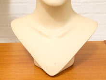 Load image into Gallery viewer, A beige mannequin bust display stand on a wooden tabletop against a white brick wall background.