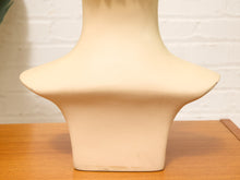 Load image into Gallery viewer, A cream-colored ceramic bust or vase-like decorative object with a flared collar, displayed on a wooden tabletop against a white brick wall background.