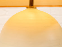 Load image into Gallery viewer, A close-up of a warm white or cream-colored dome-shaped glass or plastic light shade, glowing with a soft yellow light, with a small brass-colored metal fitting visible at the top.