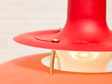 Load image into Gallery viewer, Close-up of a modern table lamp with a bright red conical shade, a wide red flared rim, and a warm orange base, featuring brass-colored metal support rods and a lit bulb inside.