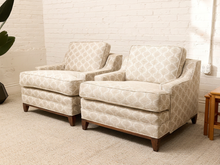 Load image into Gallery viewer, Two matching upholstered armchairs with a beige and white geometric trellis pattern and dark wood legs, shown in a bright room with a white brick wall and carpet.