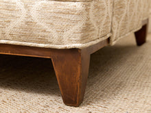 Load image into Gallery viewer, Close-up detail of an upholstered furniture piece showing a cream and beige textured fabric cushion, a dark brown wooden leg, and a woven natural-fiber rug underneath.